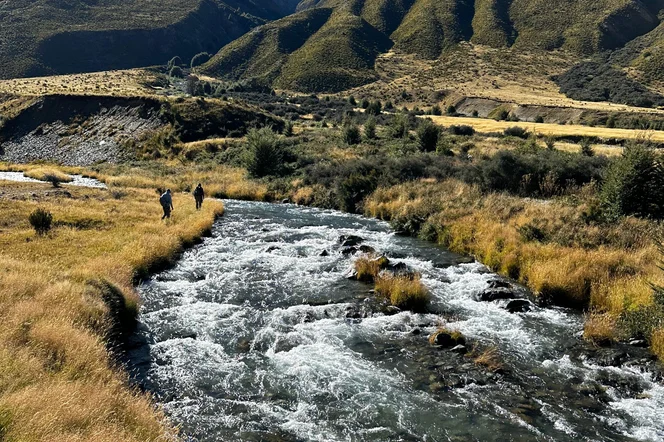 Hikers walking alongside a coursing river in a valley.
