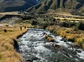 Hikers walking alongside a coursing river in a valley.