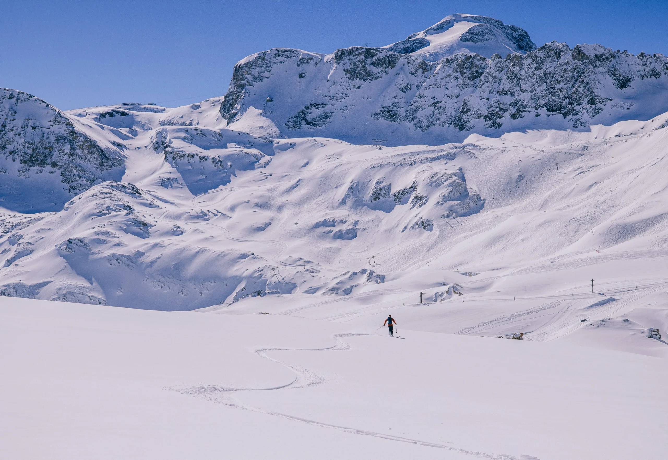 A person skiing across a range with ski lifts and mountain in the distance.