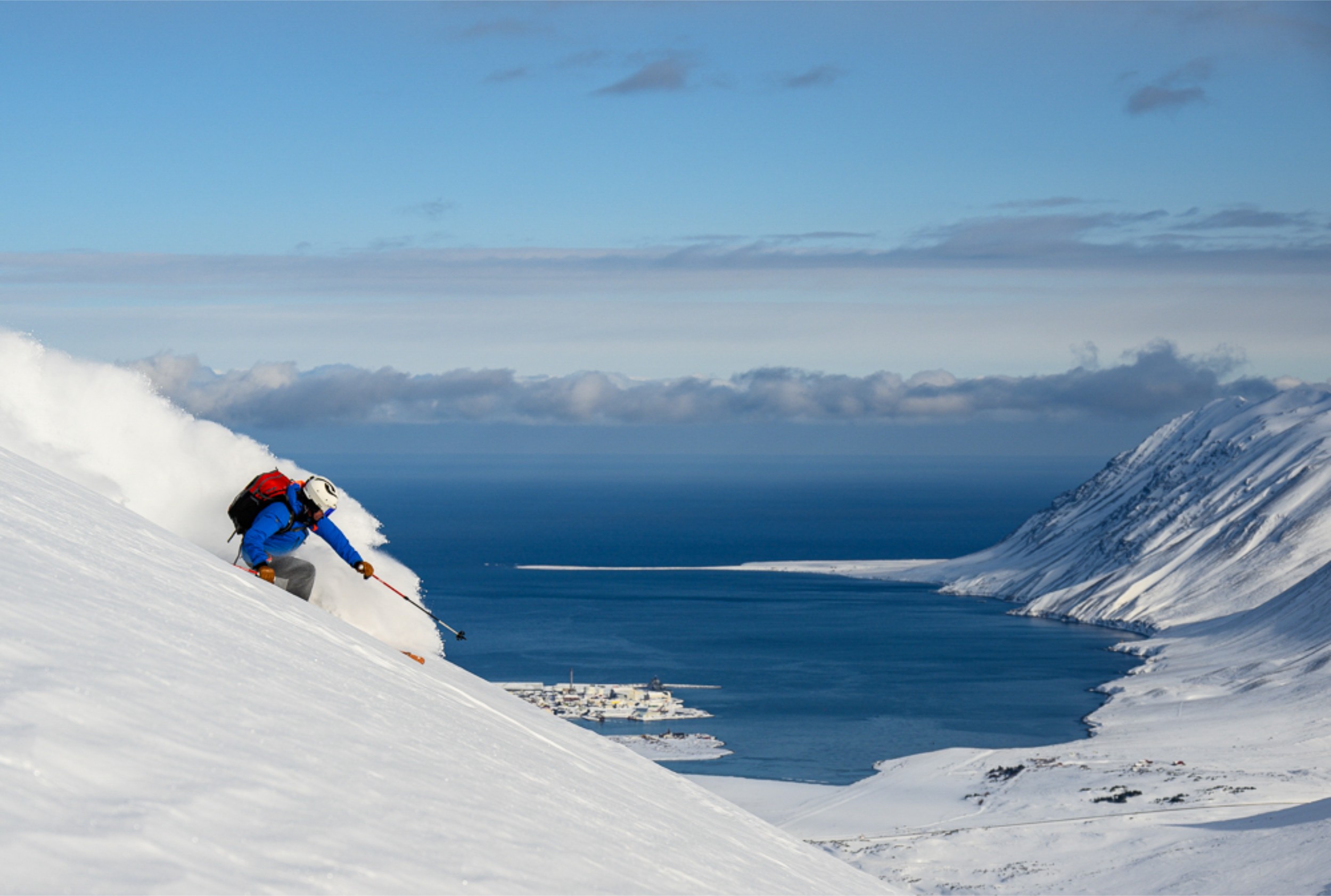 A skier headed downhill on a mountain with a view of the ocean behind.