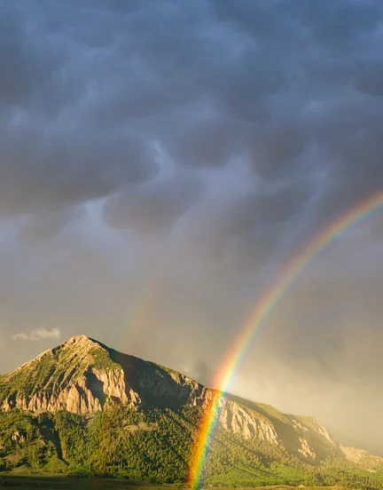 A vibrant rainbow passing in front of a lush green Colorado Mountain.