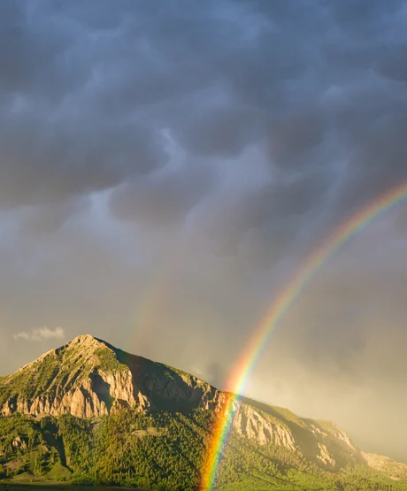 A vibrant rainbow passing in front of a lush green Colorado Mountain.