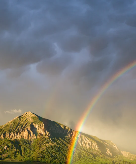 A vibrant rainbow passing in front of a lush green Colorado Mountain.