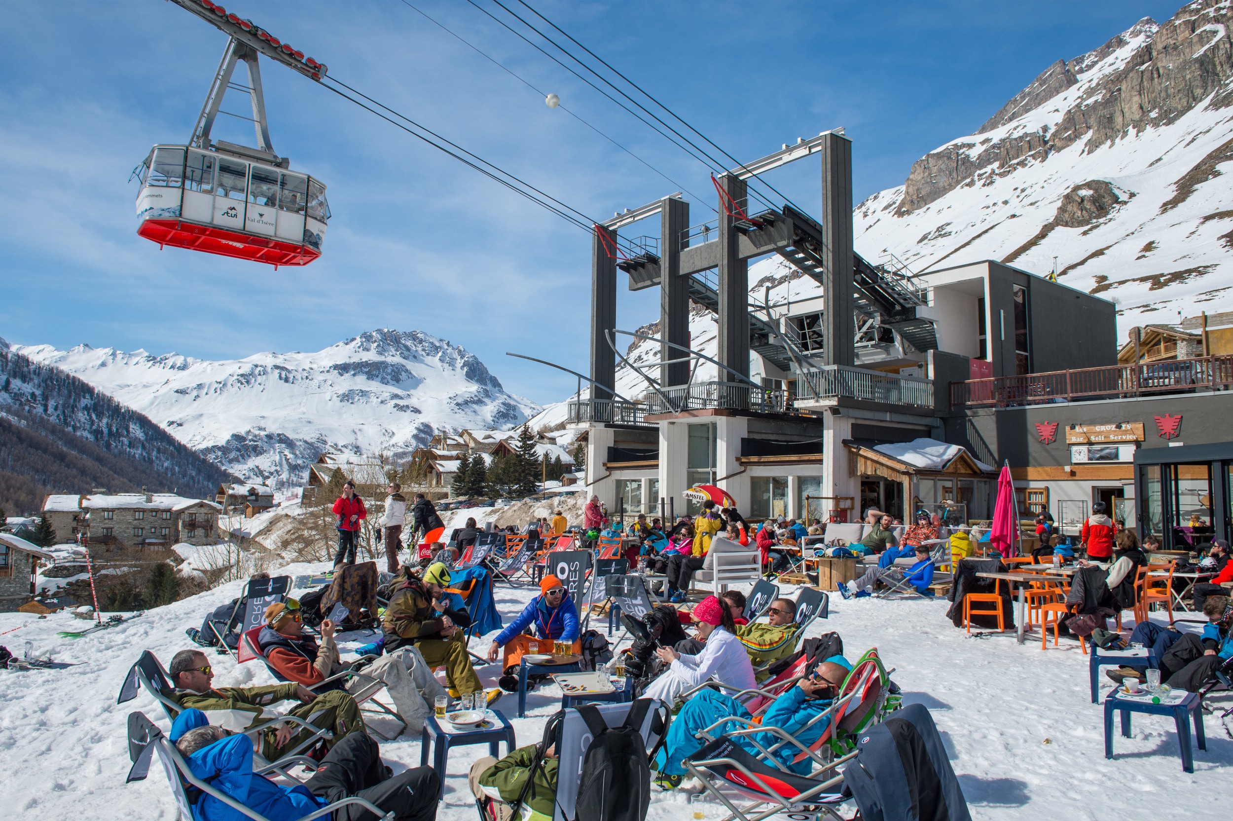 A large group of skiers hanging out at the bottom of a ski lift at a lodge.