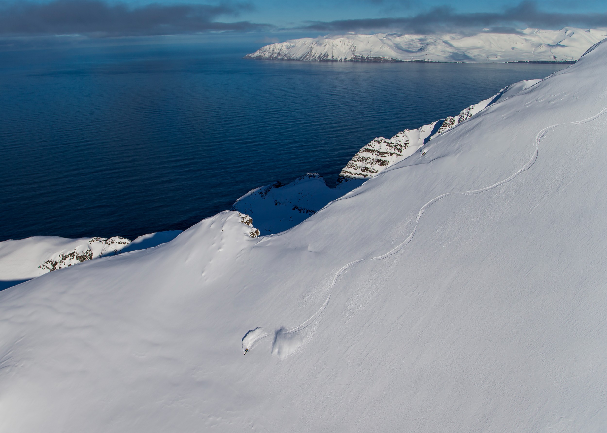 A skier carving down a mountain in powdery snow at ocean's edge.