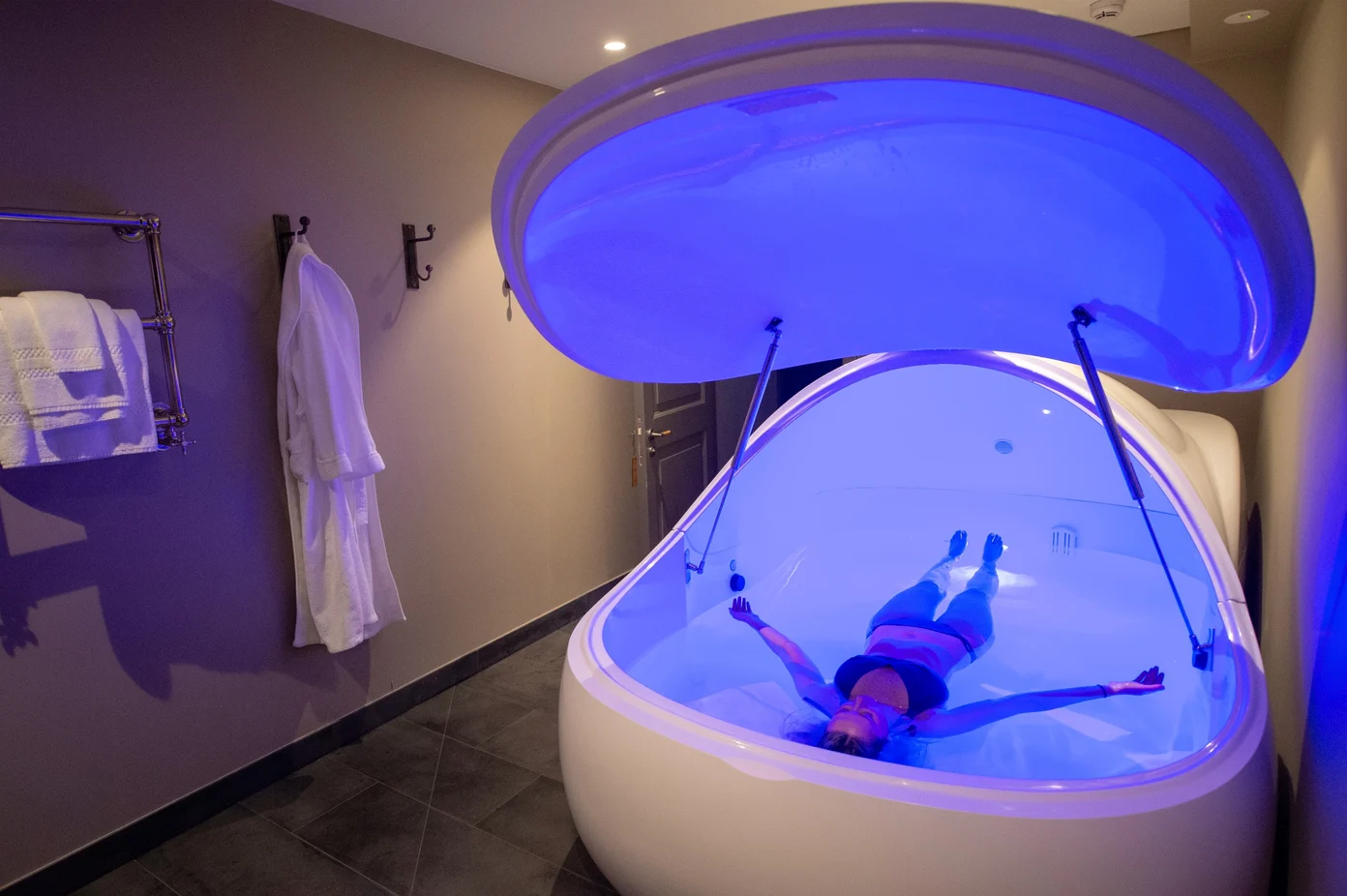 Person floating in an isolation tank with blue light.