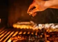 A chef's hand sprinkling salt on top of a large steak on the grill.