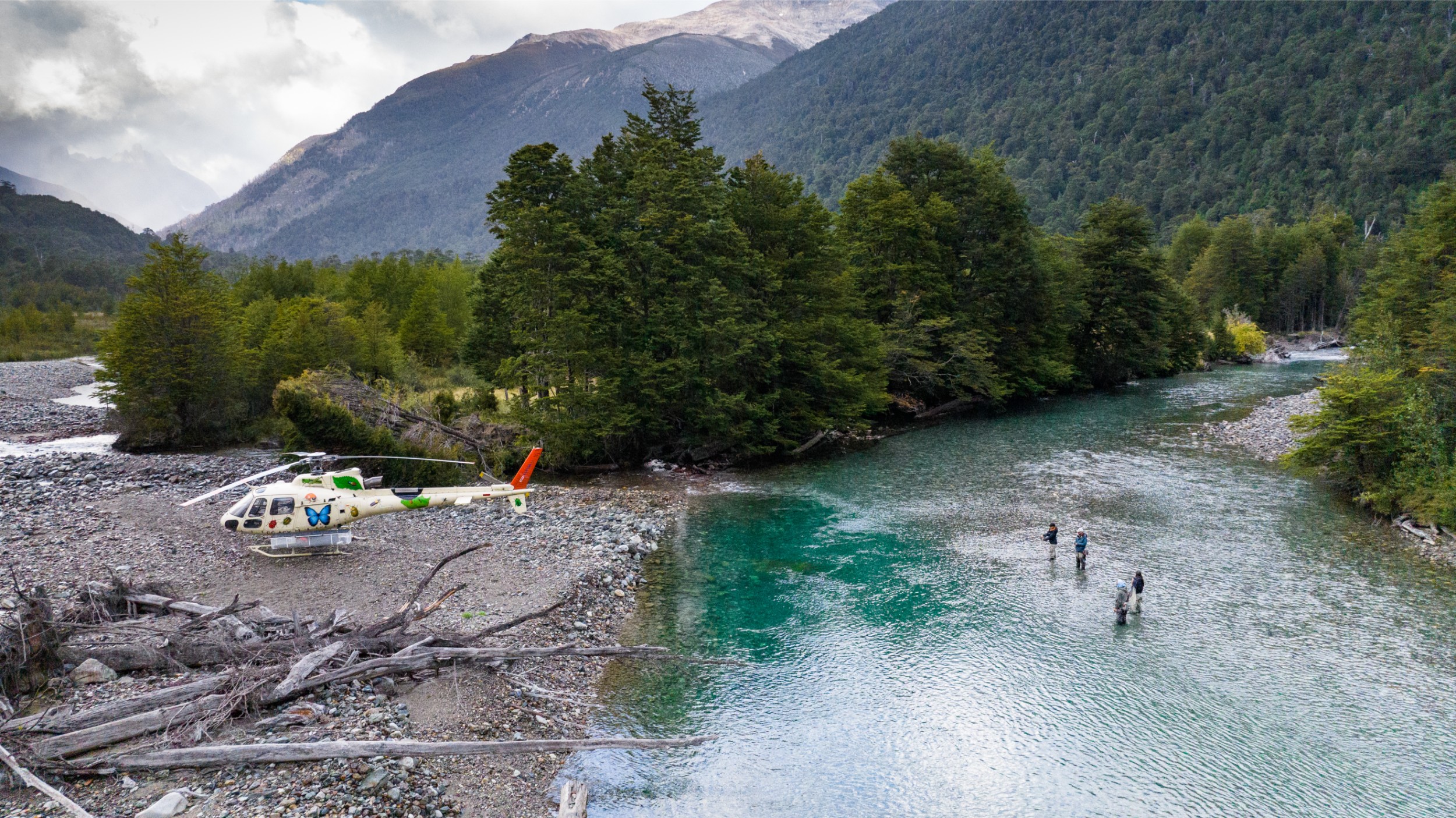 Fishers standing in water with a helicopter parked at river's edge.