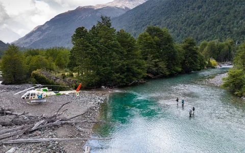 Fishers standing in water with a helicopter parked at river's edge.