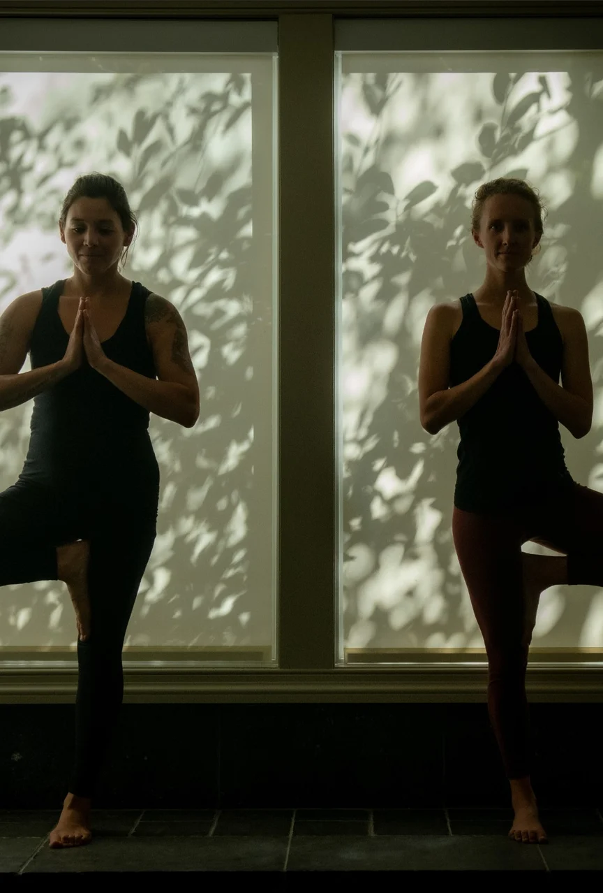 Two people holding tree pose in an intimate yoga studio.