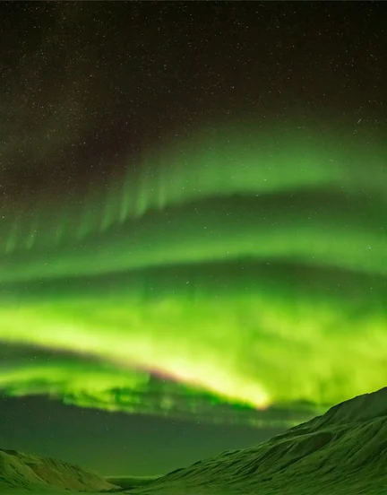A view of the northern lights through a snow-covered mountain valley.