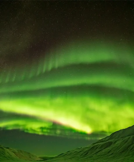 A view of the northern lights through a snow-covered mountain valley.