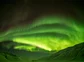 A view of the northern lights through a snow-covered mountain valley.