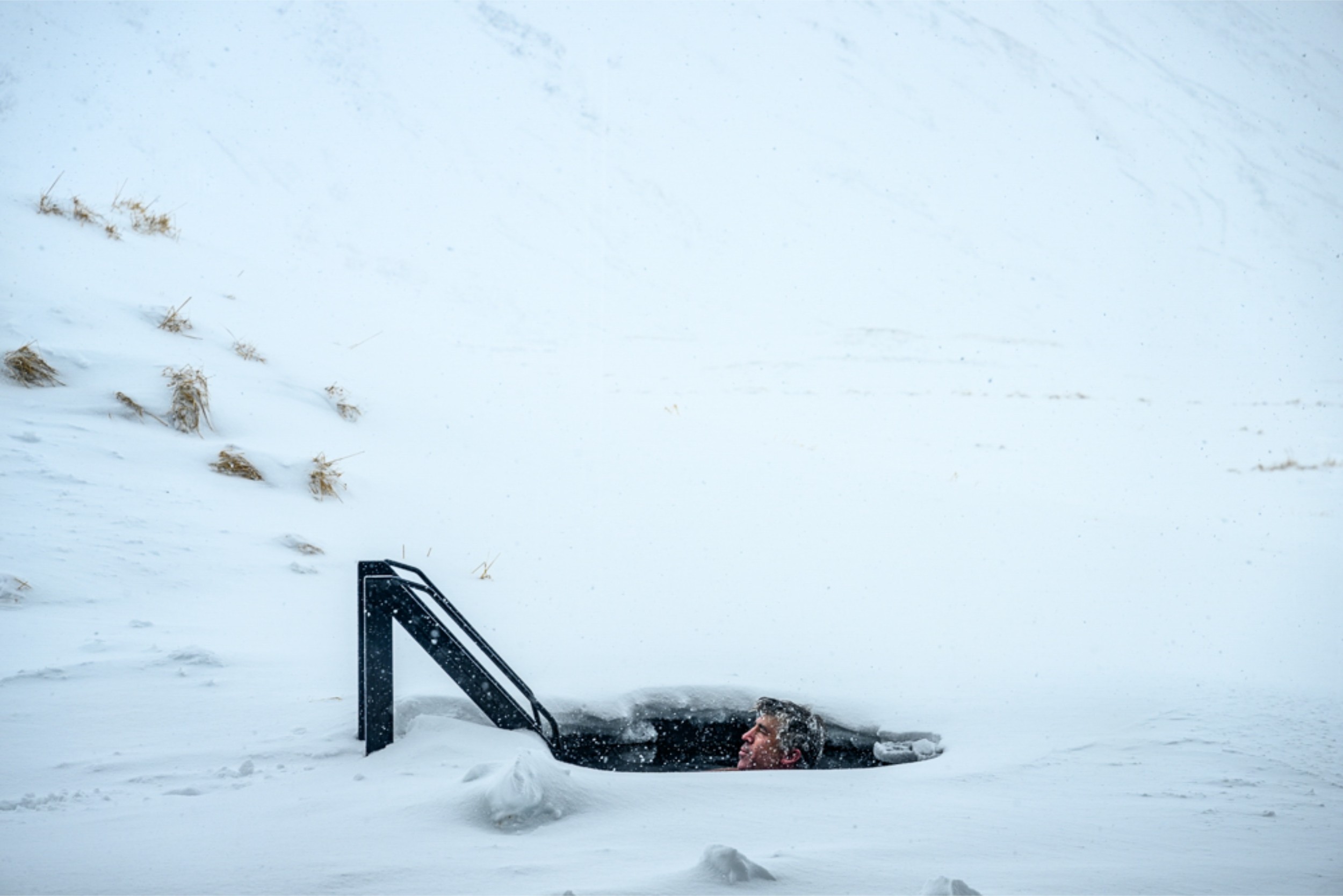 A person full submerged in a cold plunge, with snow fall.