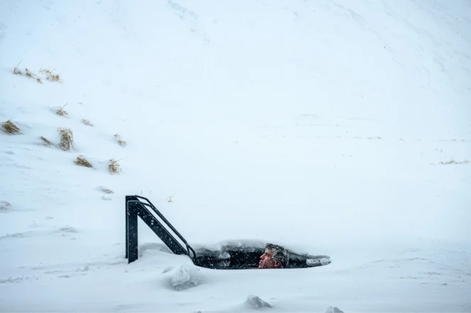 A person full submerged in a cold plunge, with snow fall.