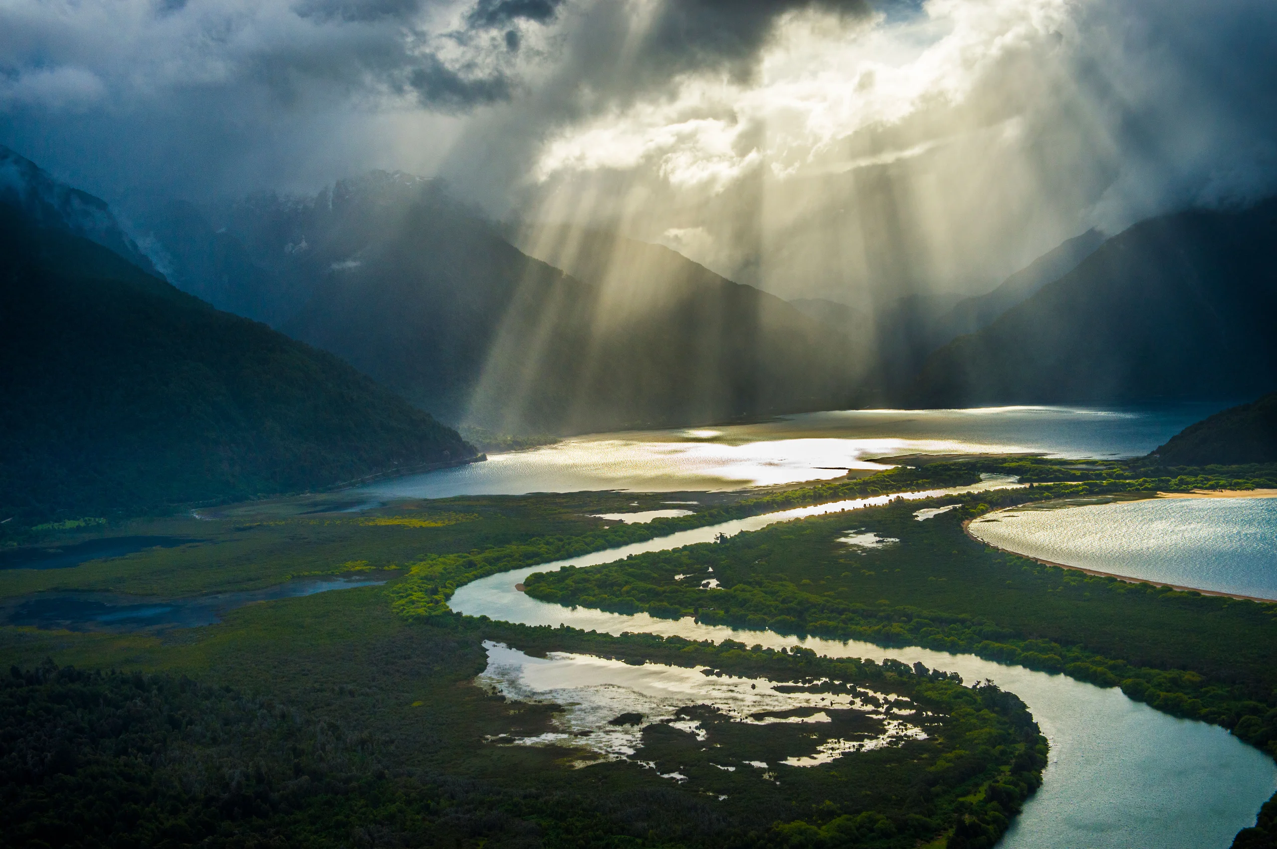 mountans in patagonia chile with sun shining through mountains and lake in front.