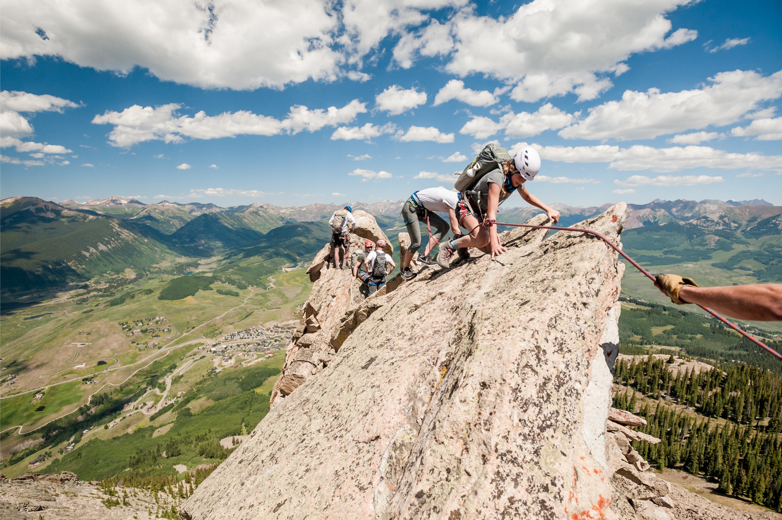 Climbers crawling across very thin and steep rocks along a mountain ridge.