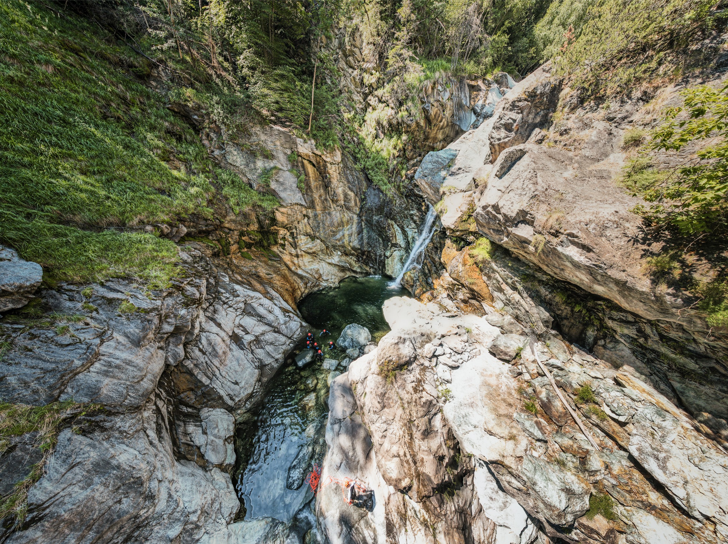 Hikers wearing helmets climbing through a watery gorge.