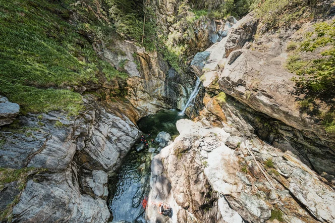 Hikers wearing helmets climbing through a watery gorge.