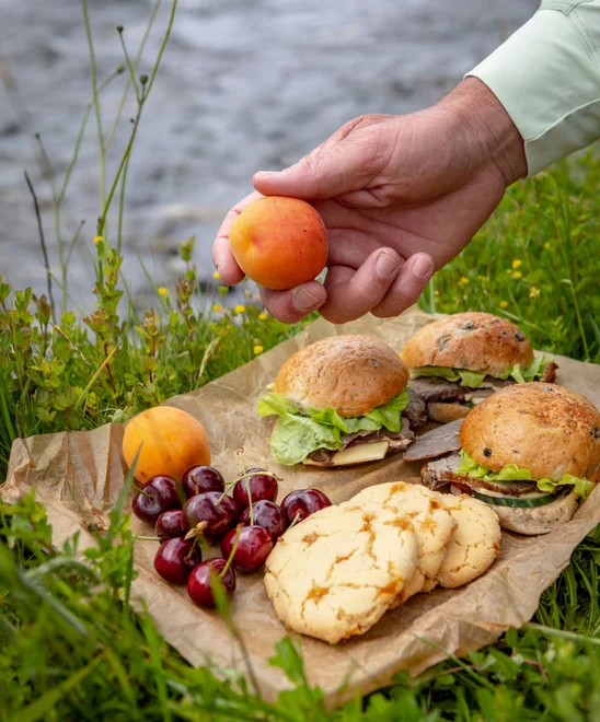 A plate of cherries, cookies, and sandwiches, on the group at rivers edge.
