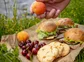 A plate of cherries, cookies, and sandwiches, on the group at rivers edge.
