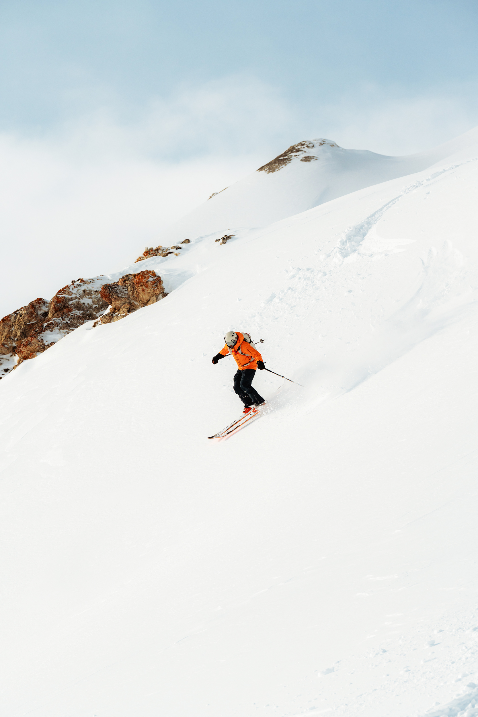 Person skiing down a mountain peak with a view of the summit in the background.