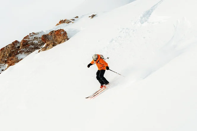 Person skiing down a mountain peak with a view of the summit in the background.