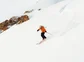 Person skiing down a mountain peak with a view of the summit in the background.