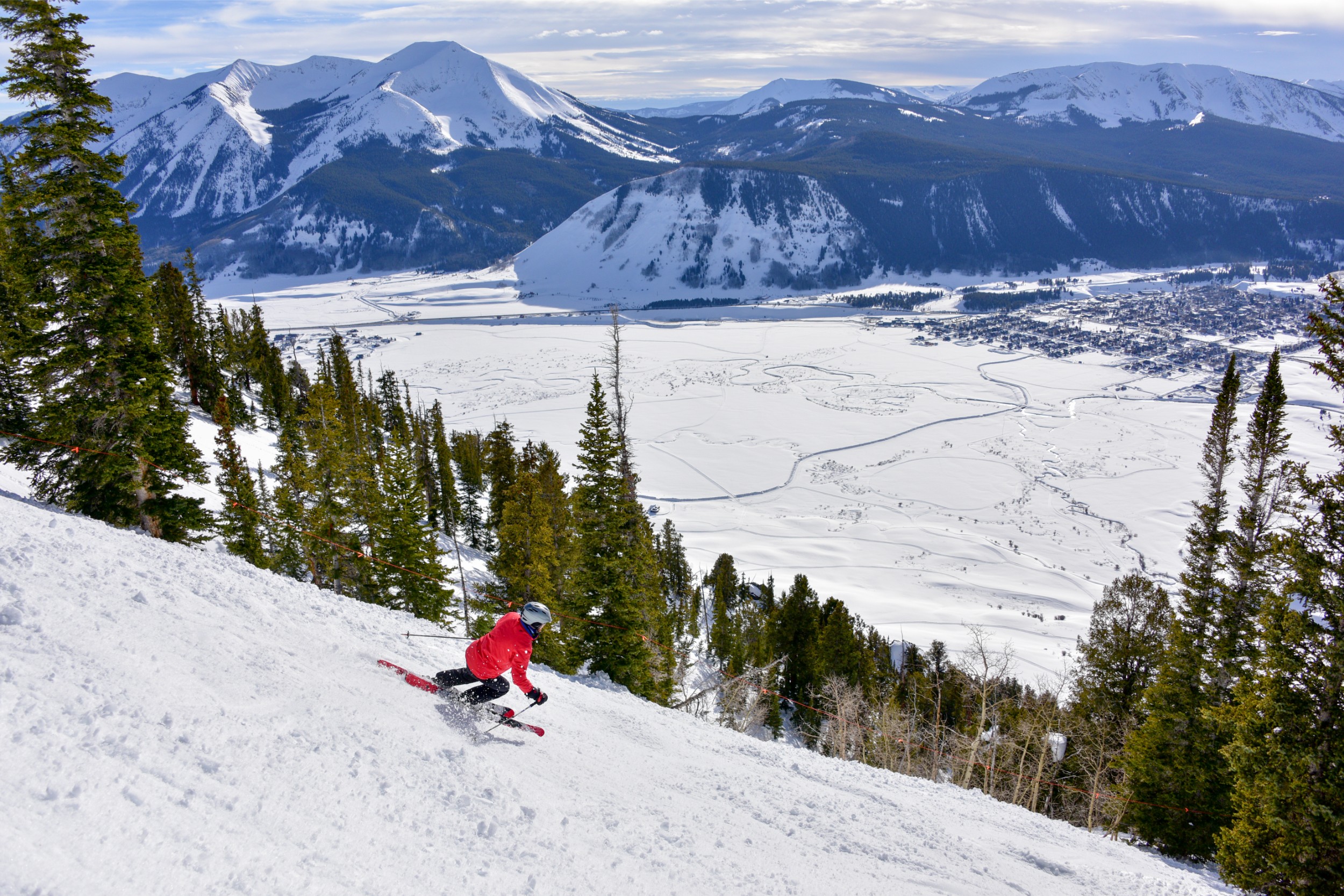 A skier going down a mountain with a view of a French town in the distance.