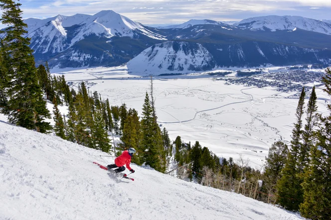 A skier going down a mountain with a view of a French town in the distance.