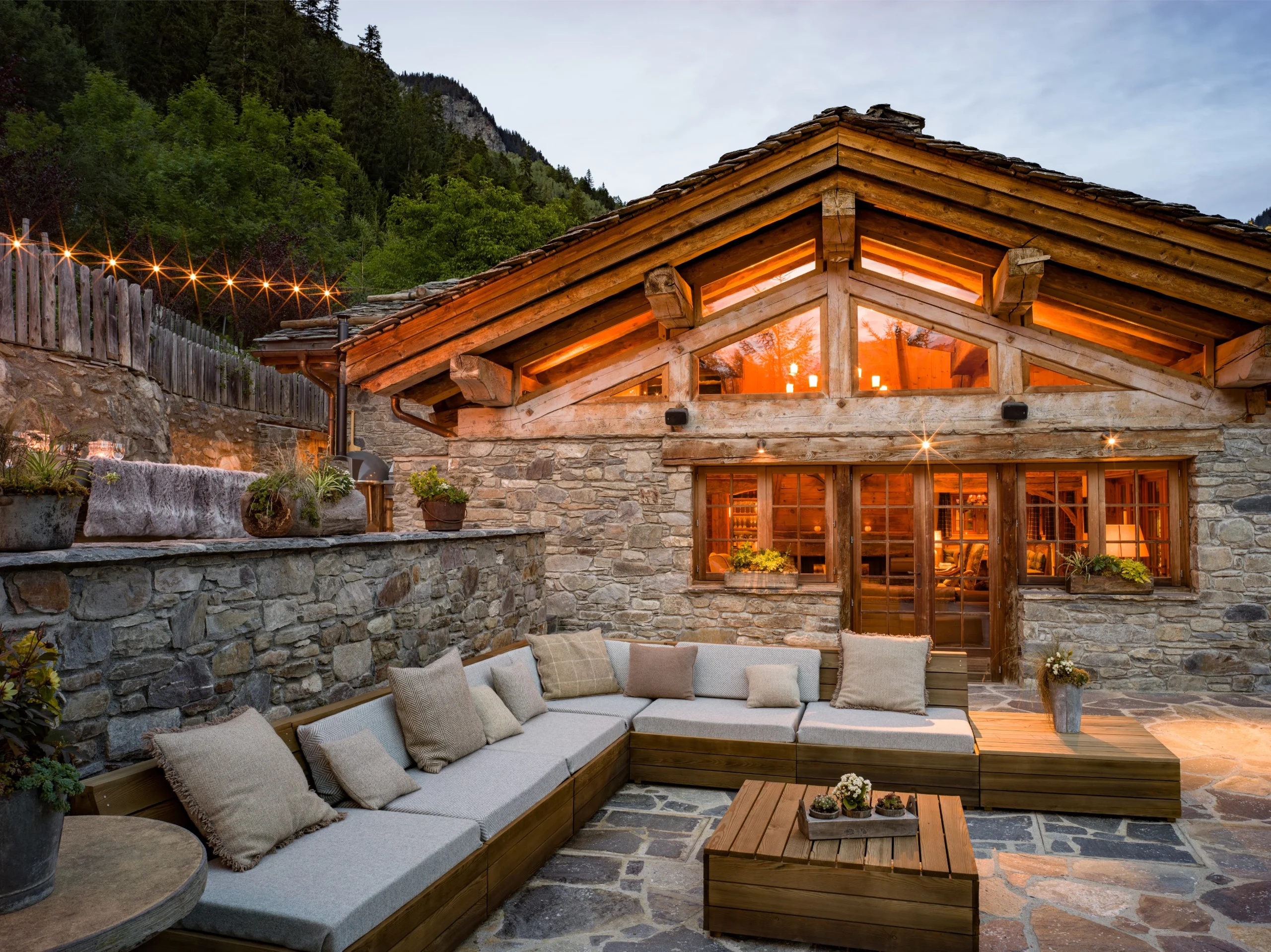 An outdoor patio with a large L-couch, pillows and lights overhead.