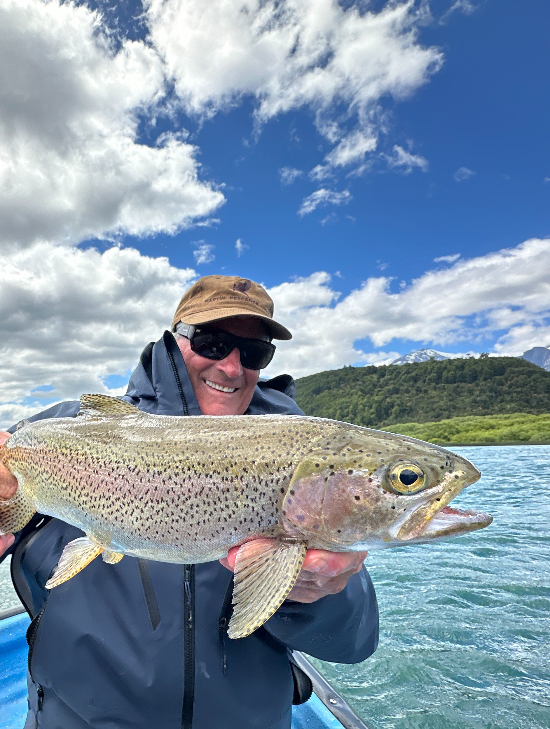 Man smiling while holding a trout on a fishing boat.