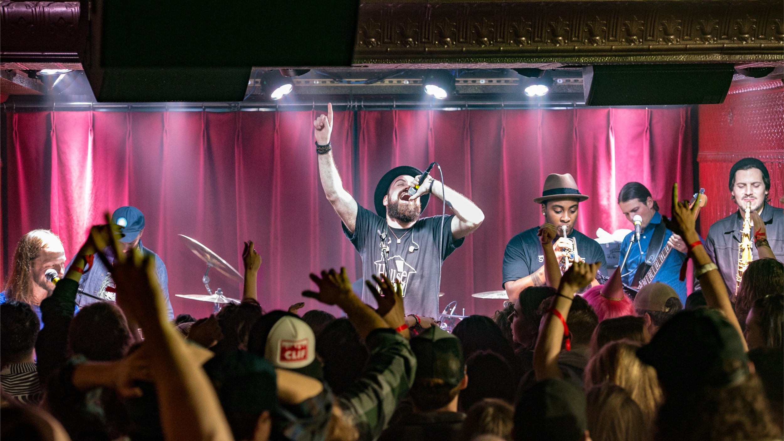 Live concert with band singing and playing and the crowd cheering in front of stage.