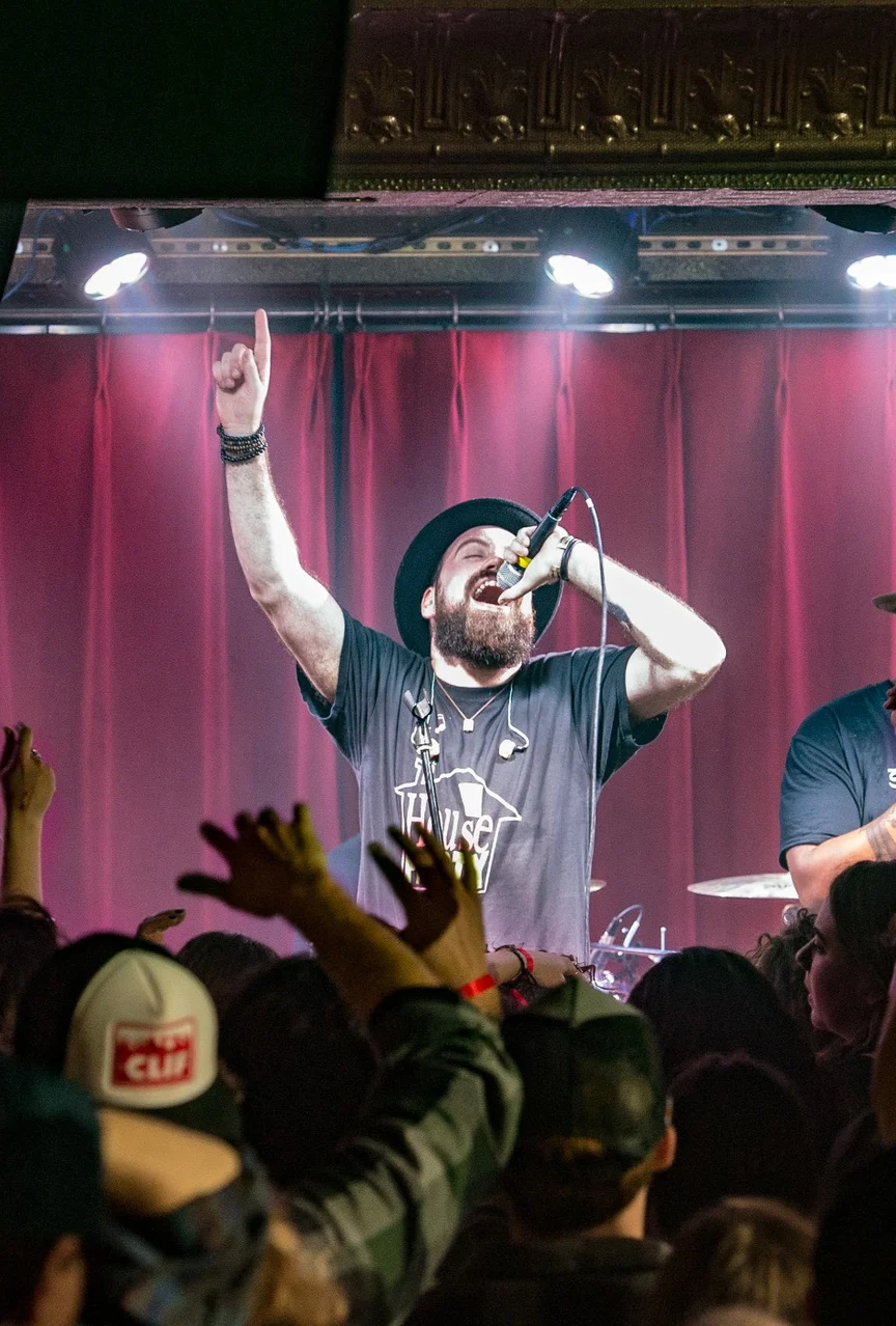 Live concert with band singing and playing and the crowd cheering in front of stage.
