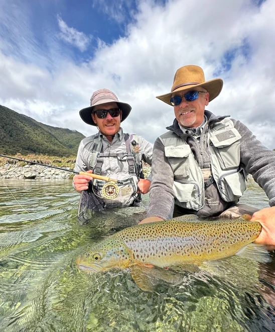 Two fishers holding a large trout in a river.