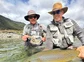 Two fishers holding a large trout in a river.