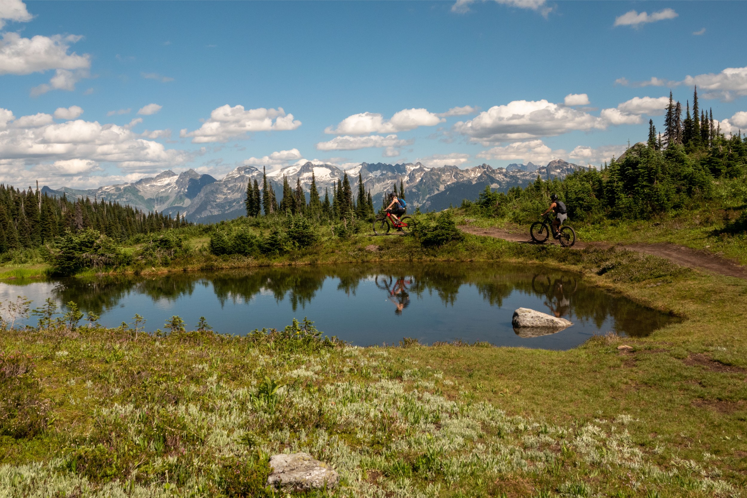 Two people mountain biking around a pond on a small mountain trail.