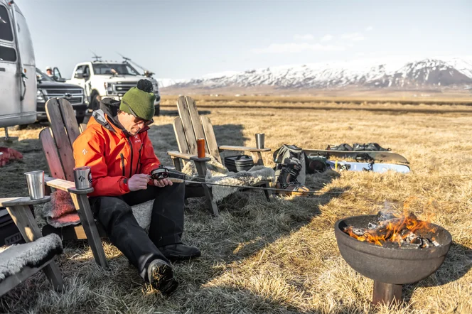 A person maintain their fishing pole by an outdoor fire pit.