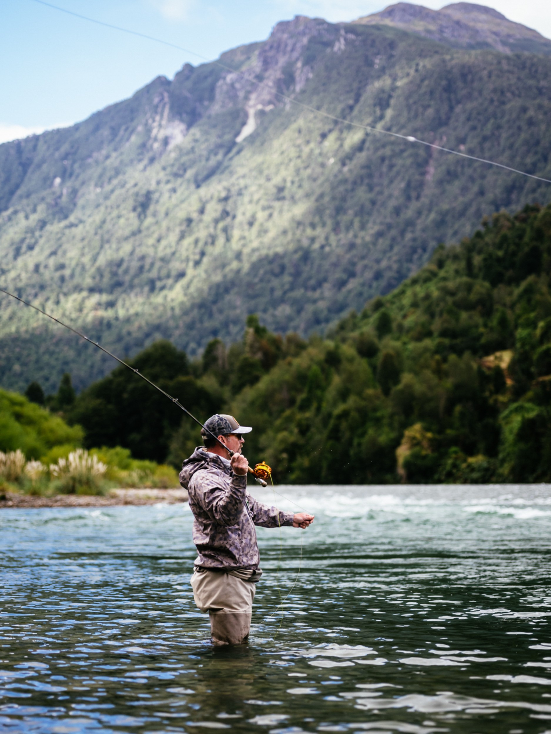 A man in wearing waders knee deep in a river, fly fishing.