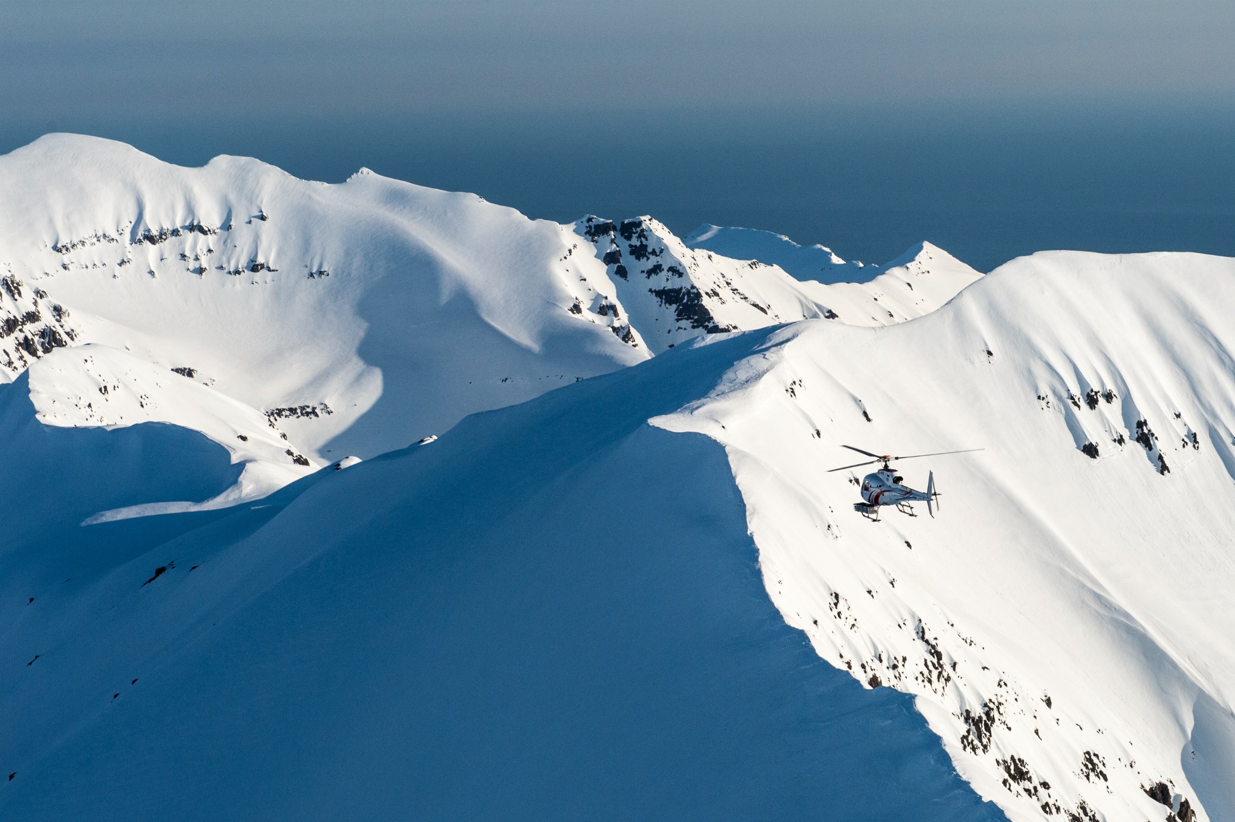 A helicopter flying over snow mountain peaks ready to drop skiers onto the mountains.