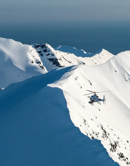 A helicopter flying over snow mountain peaks ready to drop skiers onto the mountains.
