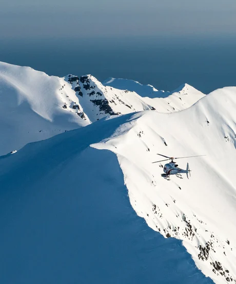A helicopter flying over snow mountain peaks ready to drop skiers onto the mountains.