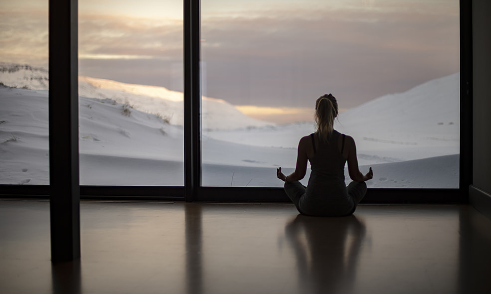 a person does yoga while looking out a window at the Icelandic landscape