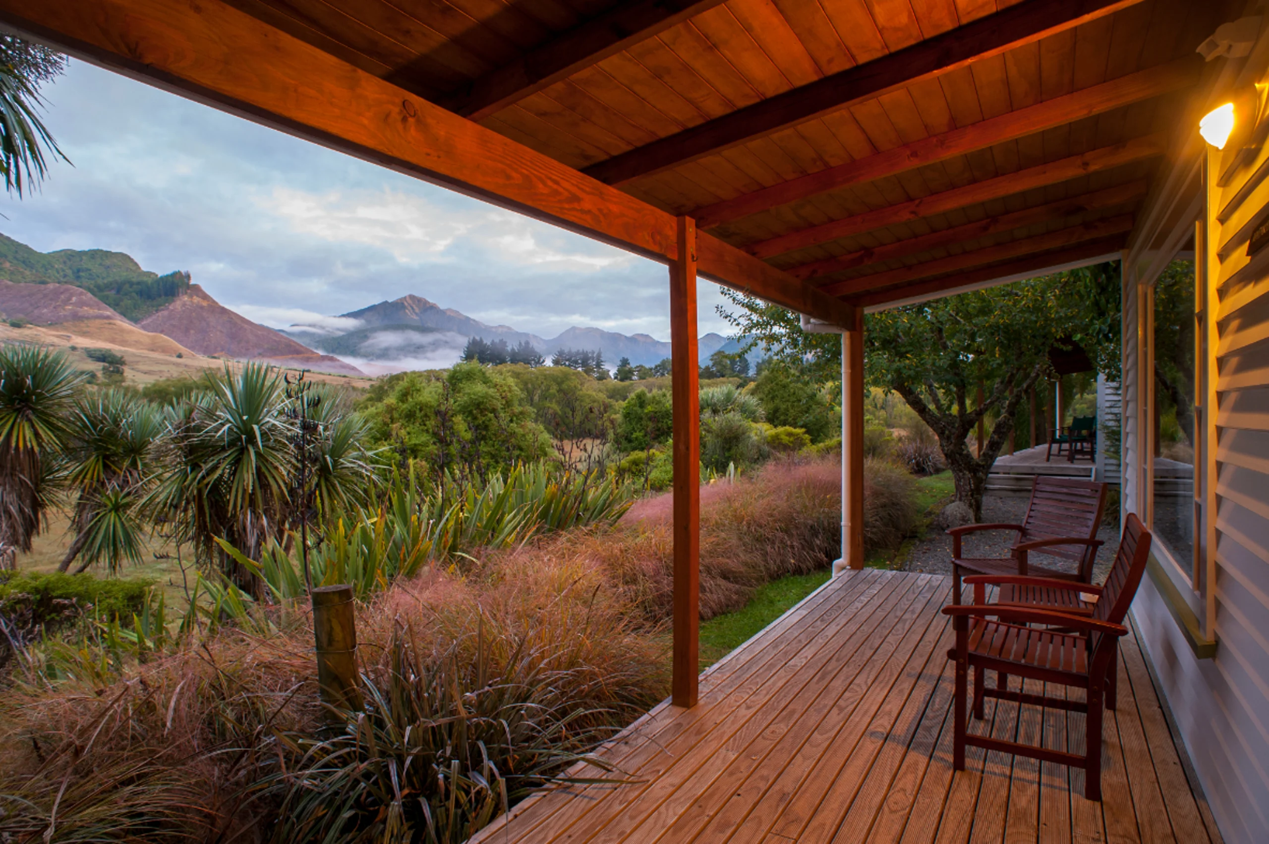 A summer evening is seen from the porch at Owen River Lodge. You can see the porch with chairs with a nice summer evening glow and greenery all around.