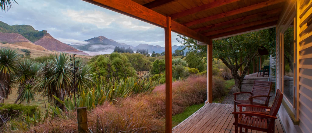 A summer evening is seen from the porch at Owen River Lodge. You can see the porch with chairs with a nice summer evening glow and greenery all around.