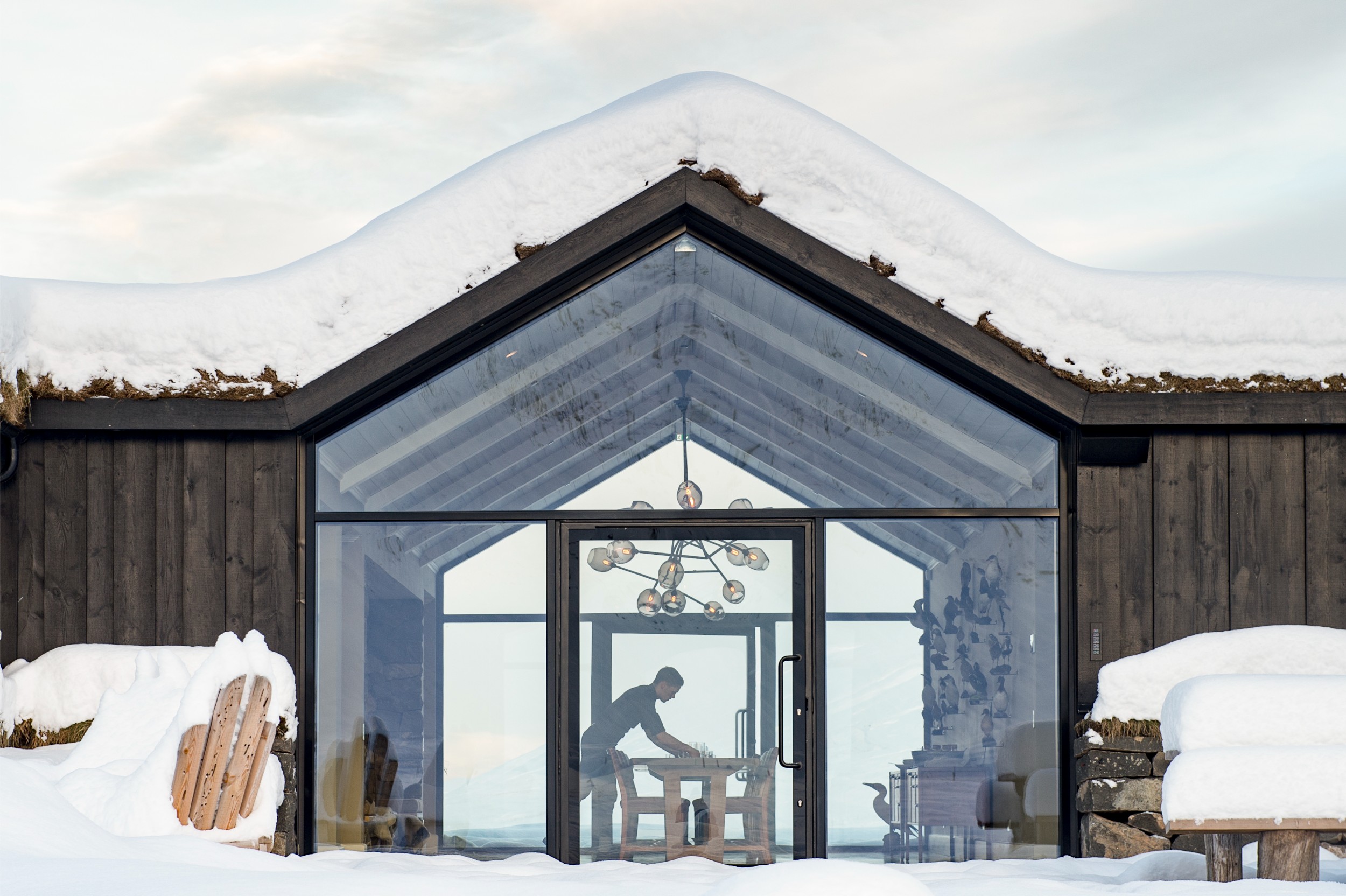 A person setting up a table in a glass dining room.