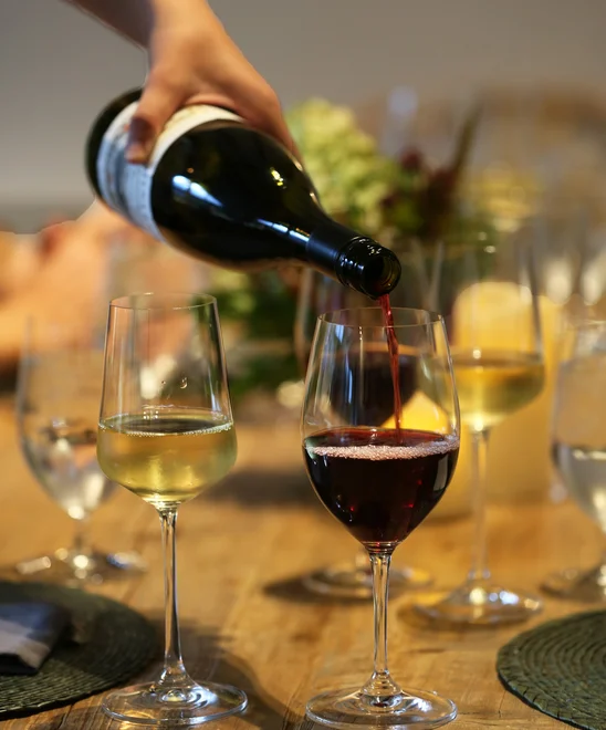Various glasses of white and red wine being poured.