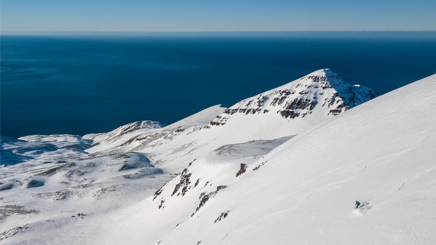 An aerial of a lone person skiing down a steep snow-covered mountain.