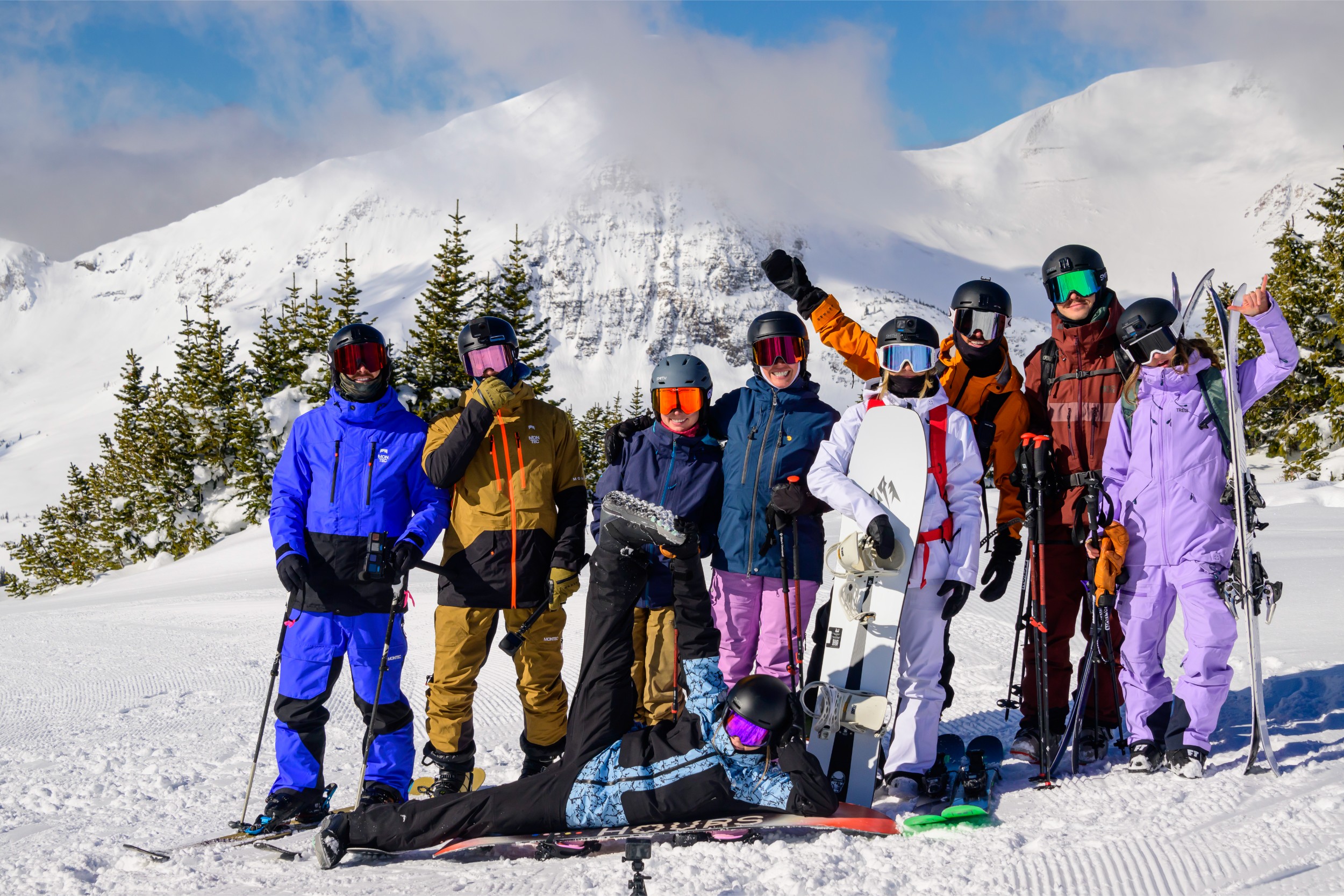 A group photo of skiers and snowboarders atop a mountain.