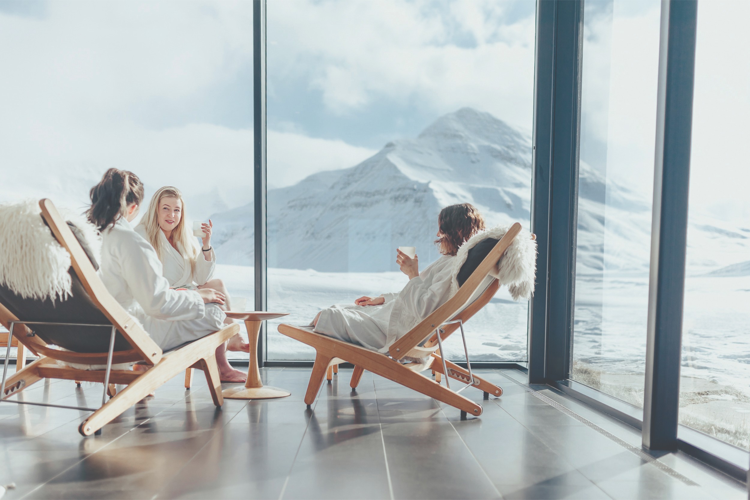 3 people enjoying drinks in spa chairs with views of a mountain.